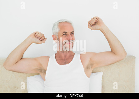 Reife lächelnder Mann streckte die Arme im Bett Stockfoto