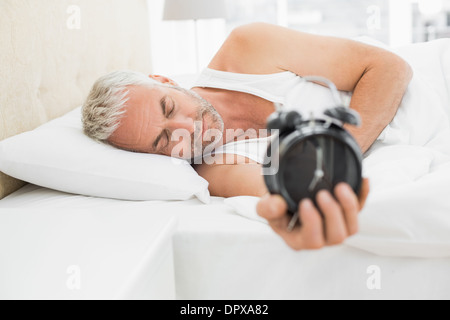 Verschlafene reifen Mann, der Wecker im Bett Stockfoto