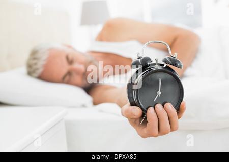 Reifer Mann streckte Wecker im Bett Stockfoto