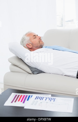 Geschäftsmann auf Sofa mit Grafiken auf Tisch im Wohnzimmer schlafen Stockfoto