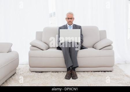 Konzentrierte Geschäftsmann mit Laptop auf dem Sofa im Wohnzimmer Stockfoto
