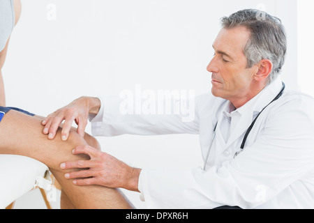 Seitenansicht des Reifen Arzt untersuchen Patienten Knie Stockfoto