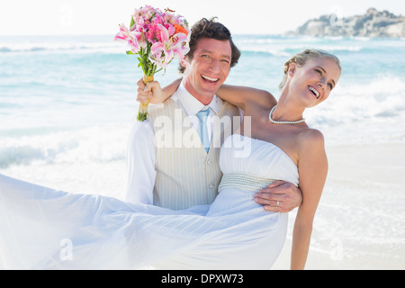 Bräutigam trägt seine hübsche blonde Frau lächelt in die Kamera lachen Stockfoto