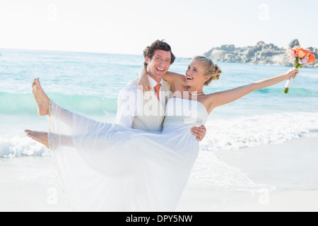 Bräutigam trägt seine hübsche blonde Frau lachen Stockfoto