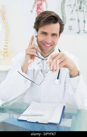 Lächelnde männlichen Arzt mit Telefon im Büro Stockfoto