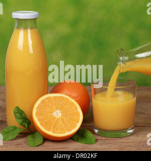 Orangen und frischer Saft ist aus der Flasche in ein Glas auf einem Holztisch gießen Stockfoto