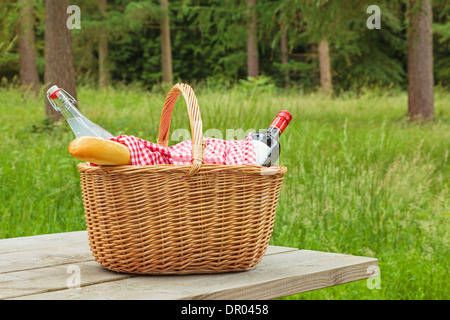 Ein Whicker Picknickkorb voller Essen und trinken auf einem Tisch in einer bewaldeten Umgebung an einem hellen Sommertag. Stockfoto