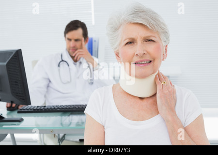 Ältere Patienten in chirurgische Kragen mit Arzt im Hintergrund im Büro Stockfoto