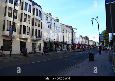 Menschen gehen vorbei an Gebäuden im Schatten entlang der Queens Road in Brighton, East Sussex, UK, auf einem frühen Sommerabend. Stockfoto