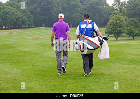 Golfer und Caddy zu Fuß in Richtung einer Kugel auf einem Par 4 Fairway. Stockfoto