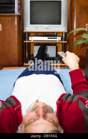 Älterer Mann mit Fernbedienung vor dem Fernseher zu Hause. Geringe Schärfentiefe mit Fokus auf Fernbedienung. Stockfoto