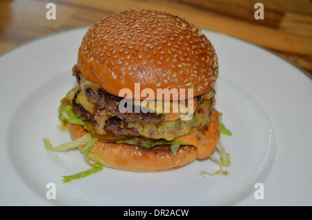 Double Cheeseburger mit Sesam Brötchen auf einem Porzellanteller serviert Stockfoto