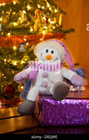 Glücklich Schneemann sitzt auf ein Weihnachtsgeschenk vor dem Weihnachtsbaum Stockfoto