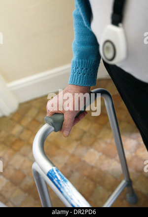 Alte Dame zu Fuß mit Hilfe einer zu Fuß Rahmen und tragen einen persönlichen Alarm. Stockfoto