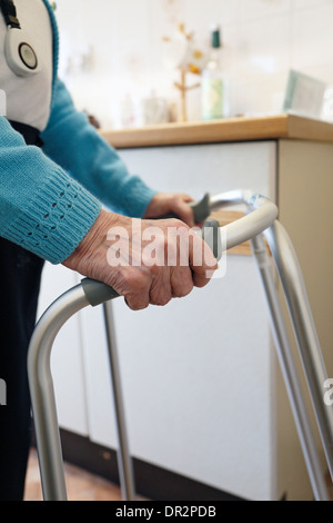 Alte Dame zu Fuß mit Hilfe einer zu Fuß Rahmen und tragen einen persönlichen Alarm. Stockfoto