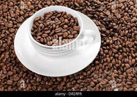 Eine Tasse voll Kaffee Bohnen umgeben von mehr Kaffeebohnen Stockfoto