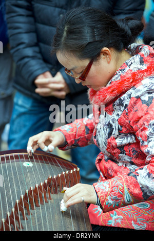 Junge orientalische Frau spielt eine chinesische Zither mit einer Masse in Mong Kok, Hong Kong. Stockfoto