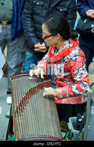 Junge orientalische Frau spielt eine chinesische Zither mit einer Masse in Mong Kok, Hong Kong. Stockfoto