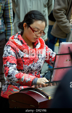 Junge chinesische Frau spielt eine chinesische Zither guzheng () mit einer Masse in Mong Kok, Hong Kong. Stockfoto