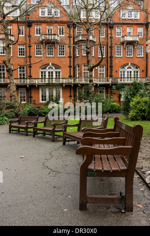 Parkbänke und dem unverwechselbaren roten Ziegeln Gehäuse der South Audley Street vom Mount Street Gardens aus gesehen Stockfoto