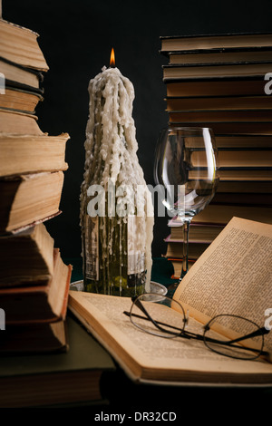 eine schmelzende Kerze in einer Flasche unter alten Büchern Stockfoto