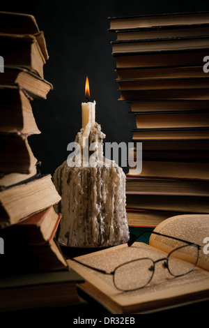 eine schmelzende Kerze in einer Flasche unter alten Büchern Stockfoto