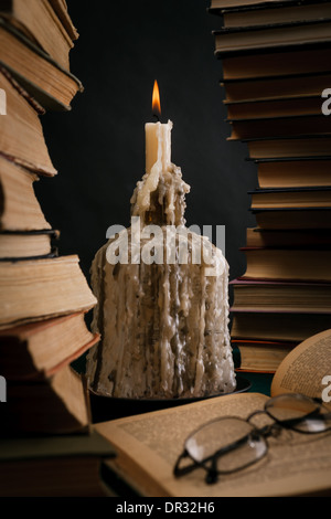 eine schmelzende Kerze in einer Flasche unter alten Büchern Stockfoto