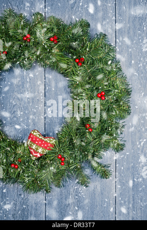 Weihnachtskranz hängend rustikale Tür mit fallendem Winterschnee Stockfoto