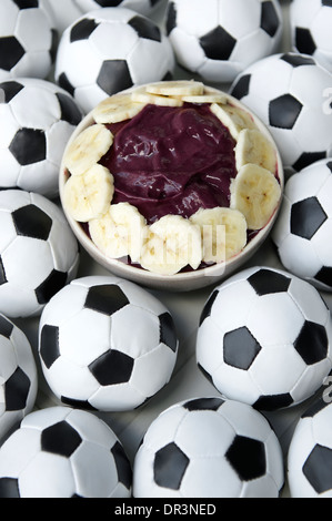 Brasilianischer Kultur auf dem Tisch verfügt über eine Schüssel mit frischen Acai mit Banane, umgeben von Fußball Fußbälle Stockfoto