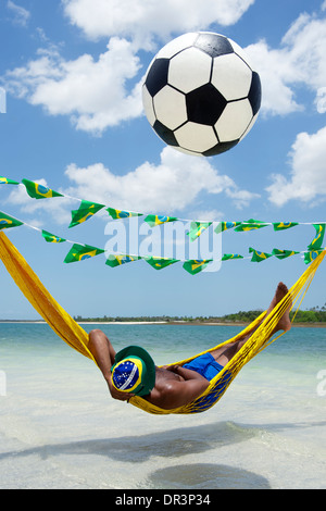 Brasilianische Fußball-Fan zum Entspannen in Strand-Hängematte mit einem schwebenden Fußball Stockfoto