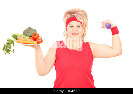 Reife Frau hält Teller mit Gemüse und eine Hantel Stockfoto