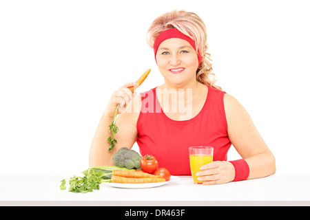 Mittlere gealterte Frau sitzend am Tisch essen Gemüse und Orangensaft trinken Stockfoto