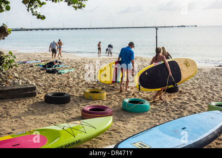 Drei Menschen tragen ihre Stand-up-Paddle-Boards in Richtung der Karibik vom Strand in St. Croix, Amerikanische Jungferninseln. Stockfoto