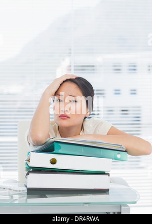 Gelangweilte Geschäftsfrau mit Stapel der Ordner am Schreibtisch Stockfoto