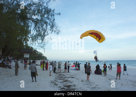 Touristen sehen auf wie ein Tandem Skydive Fallschirm landet am Strand vor 40 Thieves Bar, Diani Beach. Kenia Stockfoto