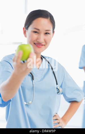 Lächelnde weibliche Chirurg hält einen Apfel im Krankenhaus Stockfoto