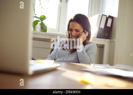 Schöne junge Frau telefonieren mit Handy während Sie an ihrem Schreibtisch sitzen. Kaukasische junge Frau im home-Office. Stockfoto