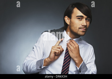 Asiatische Geschäftsmann posiert vor grauem Hintergrund. Junge männliche Model hält seine Jacke und seine Krawatte einstellen. Stockfoto
