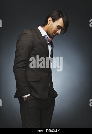 Attraktive junge Mann im eleganten Anzug stehen auf schwarzem Hintergrund. Männliche Mode-Modell mit den Händen in der Tasche nach unten Stockfoto