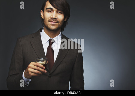 Bild des charmanten jungen Geschäftsmann mit schwarzen Kaffee. Männliches Model im Anzug hält Kaffee vor schwarzem Hintergrund Stockfoto