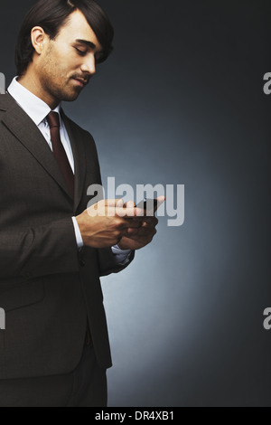 Porträt des jungen Geschäftsmann SMS mit Handy auf schwarzem Hintergrund. Asiatische Männermodel mit Handy. Stockfoto