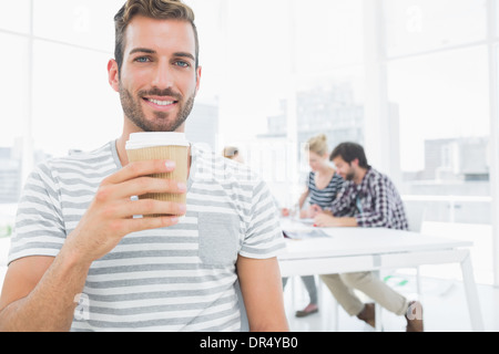 Mann, Einweg Kaffee Becher mit Kollegen im Hintergrund hält Stockfoto