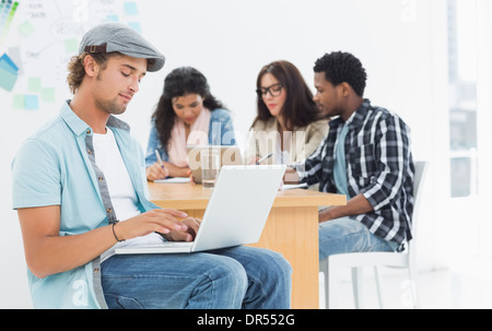 Legerer Mann mit Laptop mit Kolleginnen und Kollegen hinter im Büro Stockfoto