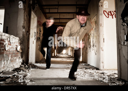 Mann läuft weg von seinem Chaser in einem verlassenen Gebäude Stockfoto