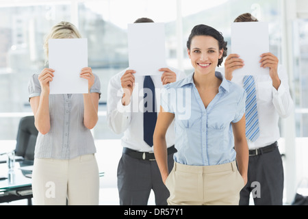 Geschäftsfrau mit Kollegen halten Blankopapier vor Gesichtern Stockfoto