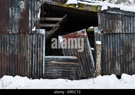 Schnee, der eine alte und rostende Wellblechscheune auf einem Bauernhof im Winter in Großbritannien bedeckt Stockfoto