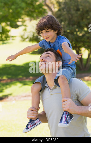 Lächelnder Mann mit Sohn auf seinen Schultern im park Stockfoto