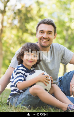 Vater und Sohn mit dem Fußball auf Rasen Inpark sitzen Stockfoto