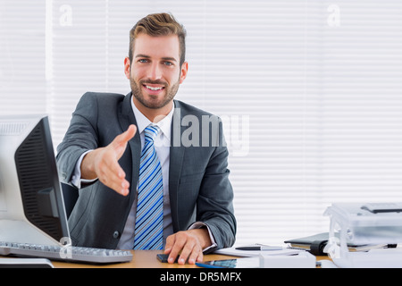 Geschäftsmann mit einem Handschlag am Schreibtisch Stockfoto