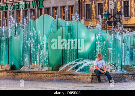 Ein junger Mann sitzt am modernen Brunnen im Breslauer Altstädter Markt oder Rynek. Stockfoto